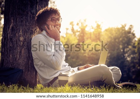 African American businessman sitting on grass and using technology.