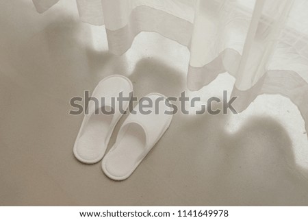 White slippers by white sheer curtains and soft sunlight, vacation concept