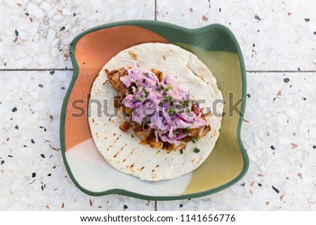Flatlay of soft pork taco with red cabbage coleslaw on a multi-coloured plate