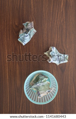 Crumpled hundred rupee notes thorwn on the garound and dustbin. A conceptual image for 'wasting money' or 'bad financial planning'