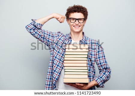 Young joyful strong student holds many books on his hand isolated on light gray background