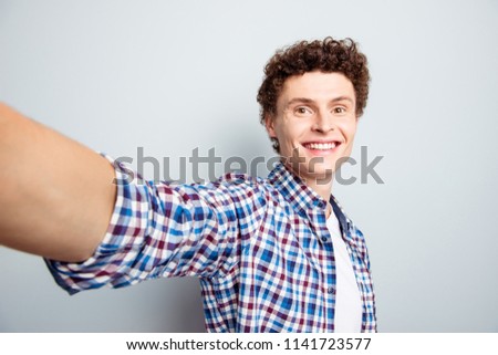 Portrait of handsome man making selfie on front camera of smartphone isolated on light gray background