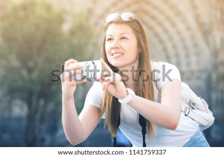 Happy girl holding phone in hands and photographing in the city
