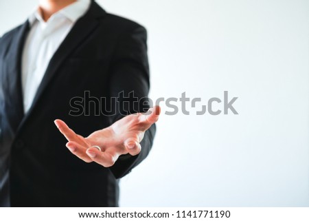 Young business man is standing and show posture open hand isolated on white background. Businessman in black suit giving empty palm.