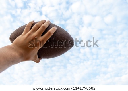 Man holding a football against the sky one handet .