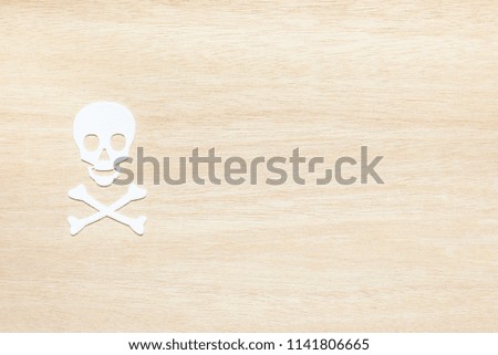 Danger and caution or risk concept : Top view of white plastic cut in skull and crossbones shape on wood background with blank space, template for putting text e.g important notice, alarm or alert etc
