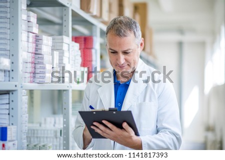 Portrait of mature male pharmacists working in modern drugstore. Medical factory supplies storage indoor with male pharmacists. Pharmacist man in the warehouse holding boxes with drugs in hands