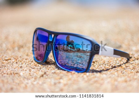 Reflection in glasses. Young couple in love lay on the sand on a sea beach on a summer day. They are happy. On vacation they travel. In the photo there is an object with a reflecting surface.
