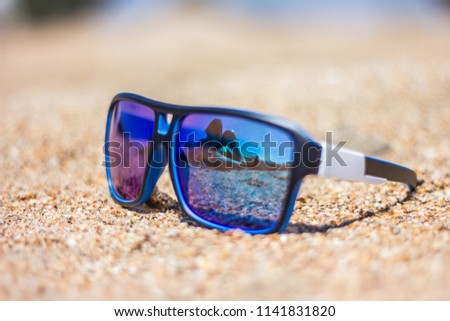 Reflection in glasses. Young couple in love lay on the sand on a sea beach on a summer day. They are happy. On vacation they travel. In the photo there is an object with a reflecting surface.