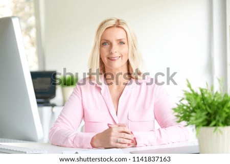 Portrait of senior financial director businesswoman looking at camera an smiling while sitting at office desk. 