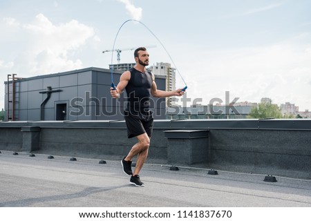 handsome sportsman training with jumping rope on roof Royalty-Free Stock Photo #1141837670