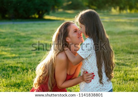 beautiful and young long-haired woman playing with her daughter embrace and caress in a summer day in the park . happy motherhood and a wonderful childhood concept