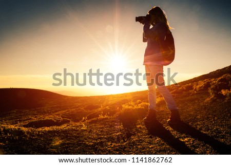 Woman hiker with backpack takes picture of the landscape in mountains during golden hour