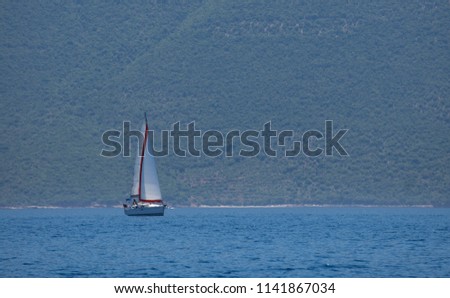 Yacht sailing from left to right across horizon with green mountain in background