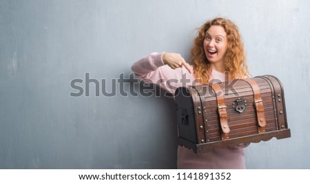 Young redhead woman holding vintage chest very happy pointing with hand and finger Royalty-Free Stock Photo #1141891352