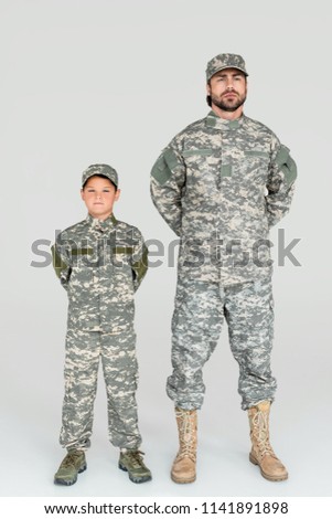 father and son in military uniforms looking at camera on grey background