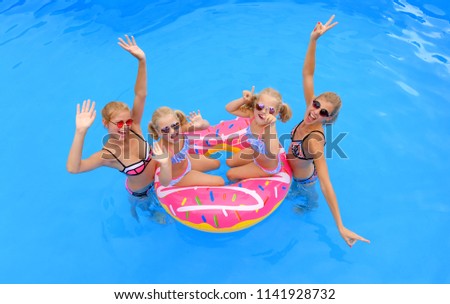 Two girls wearing bikinis gather around an 
inflatable swim ring. Two young twin sisters 
sit on the swim ring. They all are having some
summer pool fun.