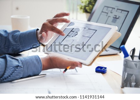 Crop hands of Indian architect working with blueprints on laptop and digital tablet