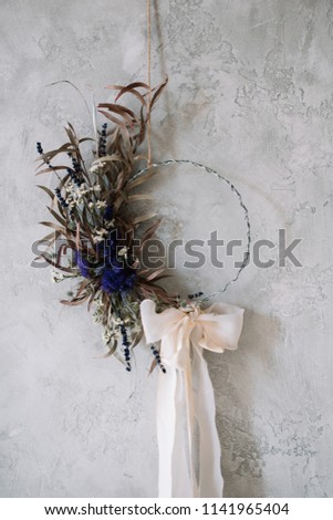 Beautiful hand made everlasting dry wreath made of dry flowers, eucalyptus tied with tender pastel coloured bow on the grey wall background