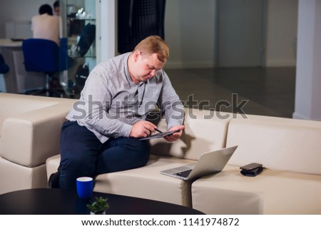 Office working concept. Man is browsing at his laptop, sitting at office on cozy white sofa