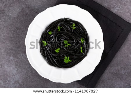 Pasta with wheat germ and black squid ink. Black pasta and parsley on a white plate.  Macro. Top view. 
