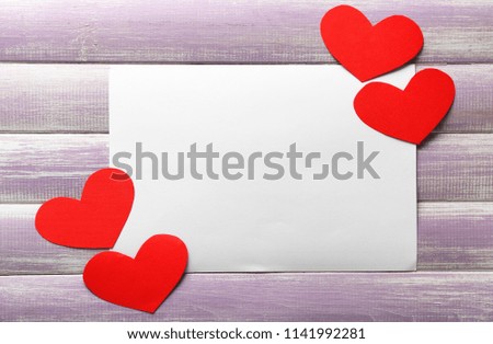 Red paper hearts and blank card on wooden background