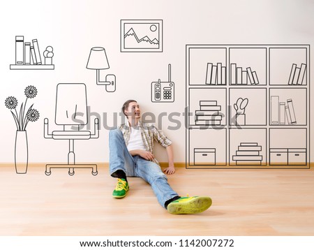 Photo of man sitting on floor with painted house flower, paintings on wall armchair, shelve, books