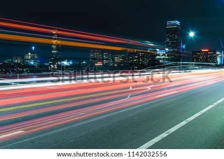 Boston skyline at night viewed from the Harvard Bridge in Boston, with light trails from cars and buses