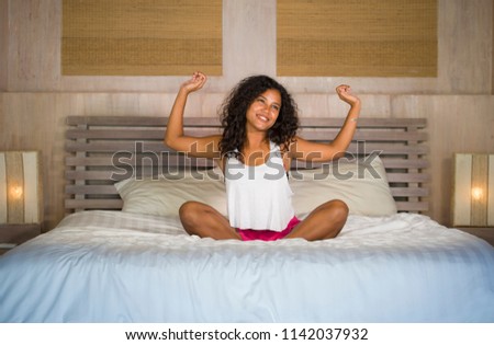 lifestyle portrait of young beautiful and happy latin American woman waking up at home bedroom in the morning stretching arms on sitting on bed smiling cheerful ready to start a new day