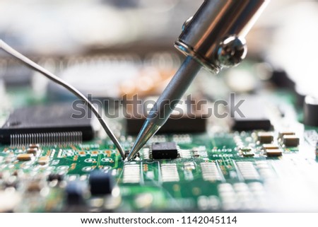 The hand holding the tin, a soldering iron solder the chip in place. Computer repair. Macrophotography. Royalty-Free Stock Photo #1142045114