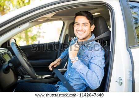 Portrait of handsome young man sitting in driving seat of car and wearing seatbelt for safety Royalty-Free Stock Photo #1142047640