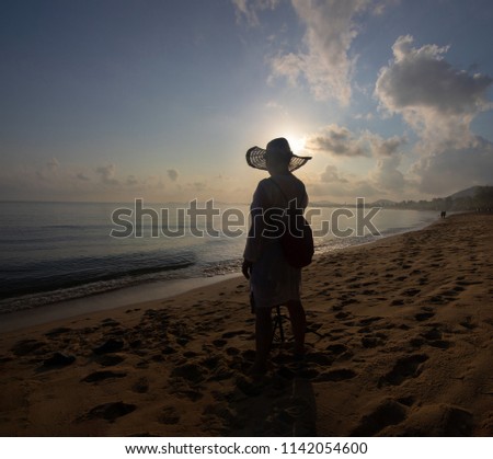 Seascape and the girl in the hat shoots a video or photo at dawn