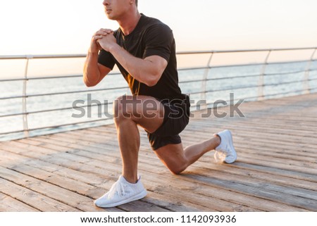 Cropped image young sportsman doing stretching leg exercises at the seaside
