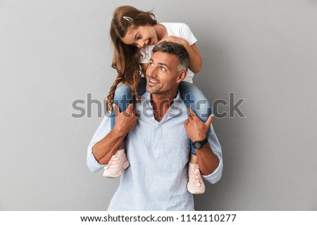 Portrait of lovely daughter smiling and sitting on the neck of her handsome father isolated over gray background Royalty-Free Stock Photo #1142110277