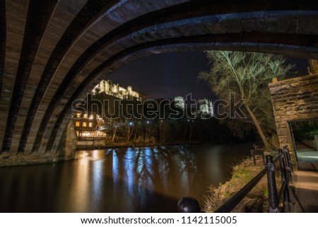 Durham Castle and Cathedral are lit up at night and are pictured framed by a stone arch of Framwellgate Bridge across the River Wear