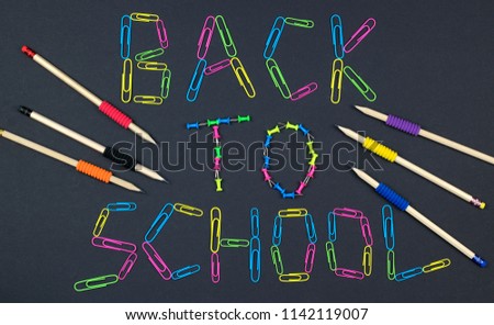 Inscription back to school on the background blackboard made of colorful paper clips and pencils.
