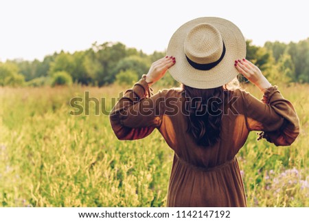 the girl in the hat is standing with her back to the field in the summer in the daylight