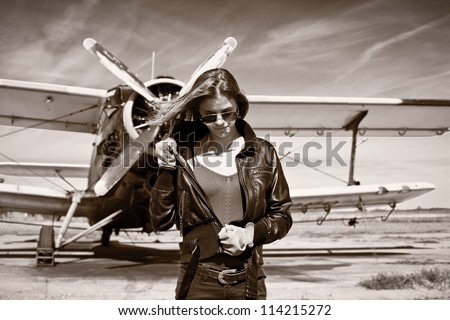 Beautiful girl in black jacket standing with aircraft behind. Retro black and white photo.