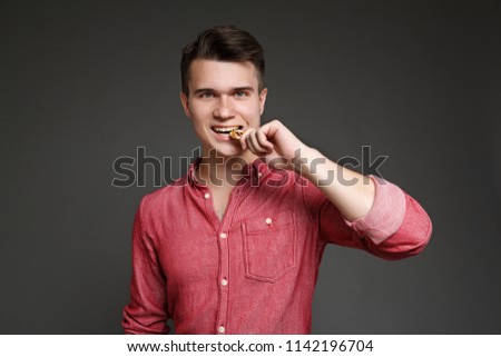 young guy bites a coin bitcoin with his teeth, checking for authenticity, isolated on a gray background. Royalty-Free Stock Photo #1142196704