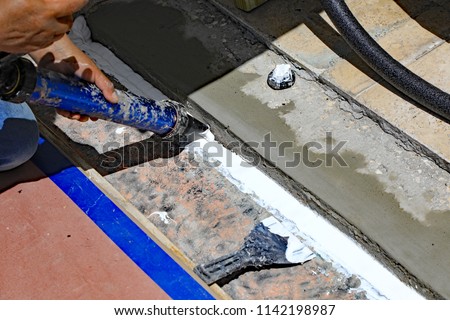 A professional construction worker is fixing an expansion joint, between two buildings, with new cement, and a flexible caulk sealant. Royalty-Free Stock Photo #1142198987