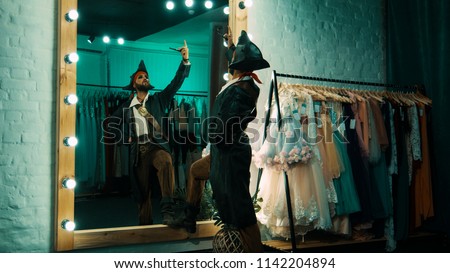 Back view of man wearing costume of pirate and standing in front of mirror in dressing room practicing scene from performance Royalty-Free Stock Photo #1142204894