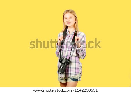 Young teenage girl holding digital photo camera with big lens & strap, taking pictures, smiling. Beautiful blond female photographer in checkered plaid shirt posing w/ dslr gear. Copy space background