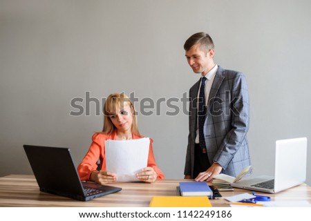 A business woman and man at a wooden office desk  working at the project on the paper and computer, grey background