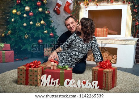 Happy family at the tree with a fireplace and gifts. Christmas eve and New year's eve. In the photo Russian letters of the word: we are a family.