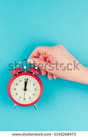 Creative flat lay concept top view of woman hand holding the red vintage alarm clock on bright blue turquoise color paper background with copy space in minimal style, template for text