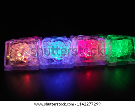 Bright and beautiful colors of different luminous ice cubes of frozen ice on a dark wooden background