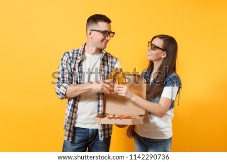 Young couple woman man sport fans in 3d glasses cheer up support team clinking beer bottles holding italian pizza in cardboard flatbox isolated on yellow background. Sport family leisure lifestyle
