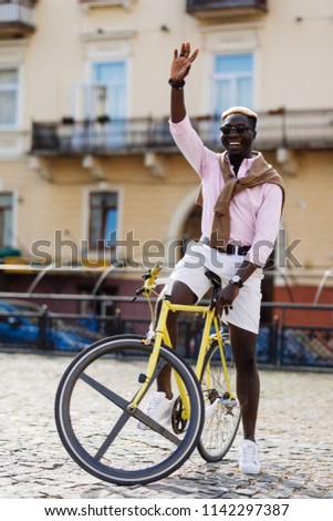 Afro young man with gear bicycle ride in the street and wave