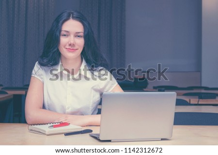 Portrait of happy smiling brunette with delicate make-up. Pretty young woman at desktop with laptop notebook and pens. Lovely female looking at camera with gladness