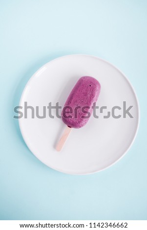 One raw vegan blueberry popsicle on white plate from above. Pastel blue background. Minimalism food photography, blogging concept. Geometric style.  Copyspace